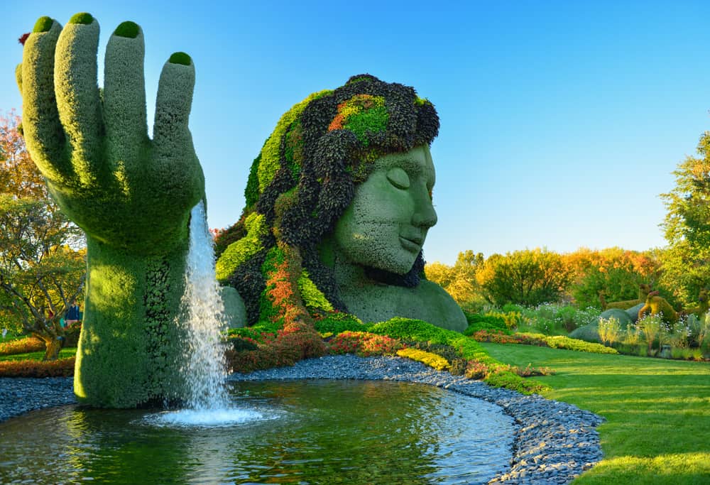 Giant green sculpture of a woman with a fountain pouring out of her hand.