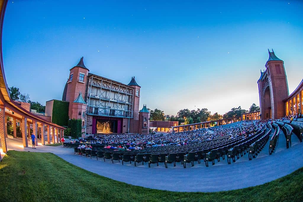 People sit in an audience watching a show on a stage outdoors.