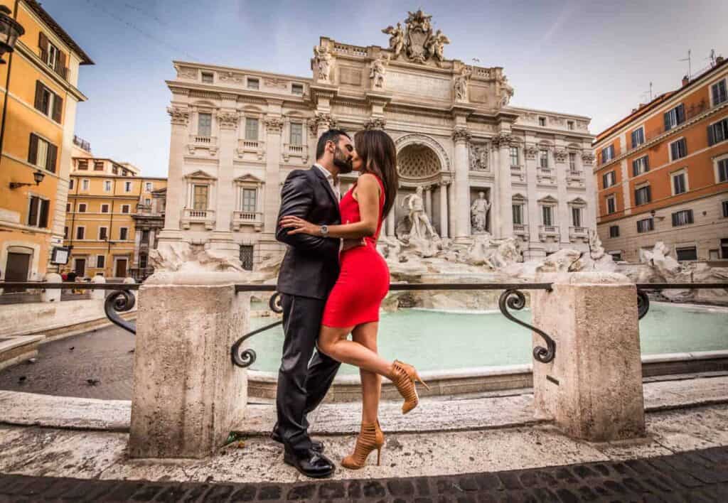 A couple stands kissing next to the Trevi fountain.