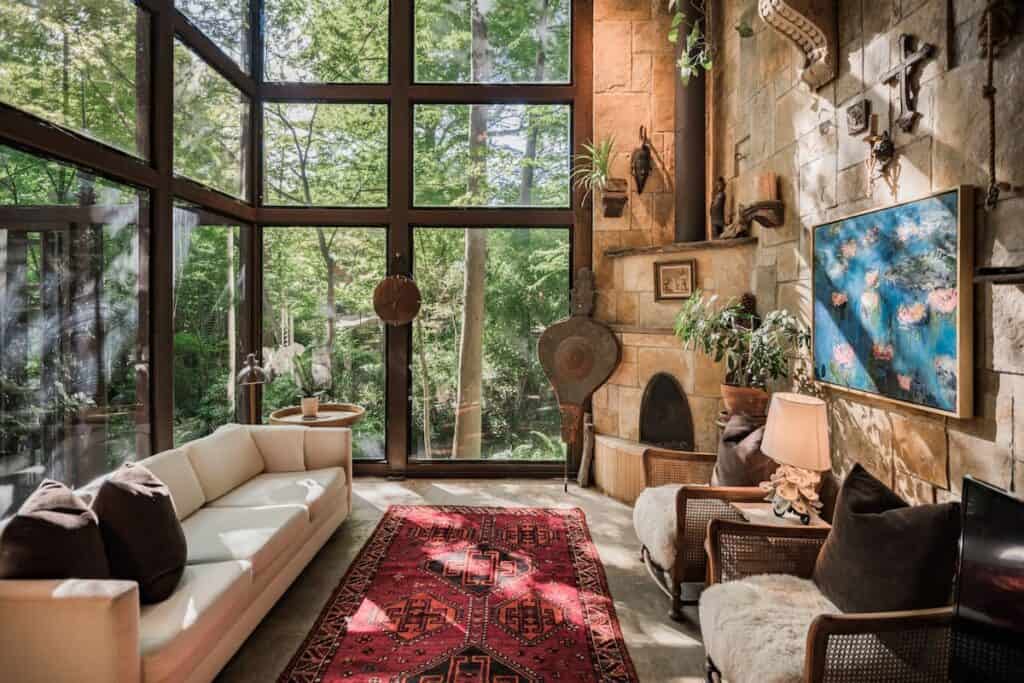 A living room has tall windows that look out to a forest.