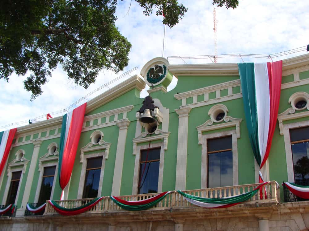 A green building is covered in Mexican flags under a blue sky.