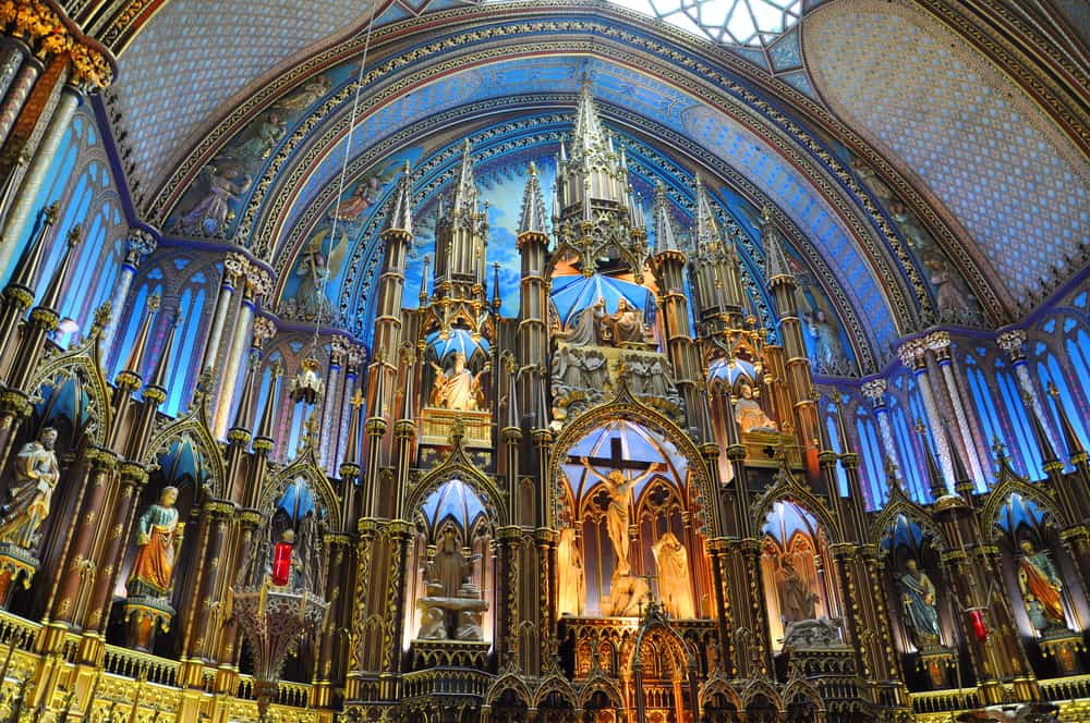 Interior of a church with a big gold structure under a painted ceiling.