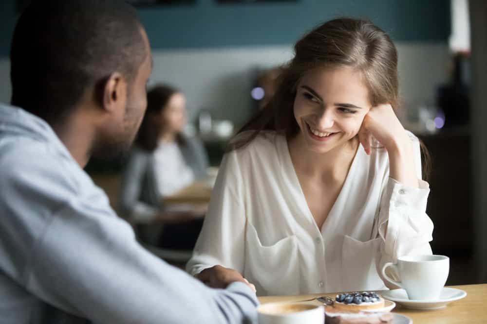 A woman smiles at a cafe while sitting at a table with her boyfriend.