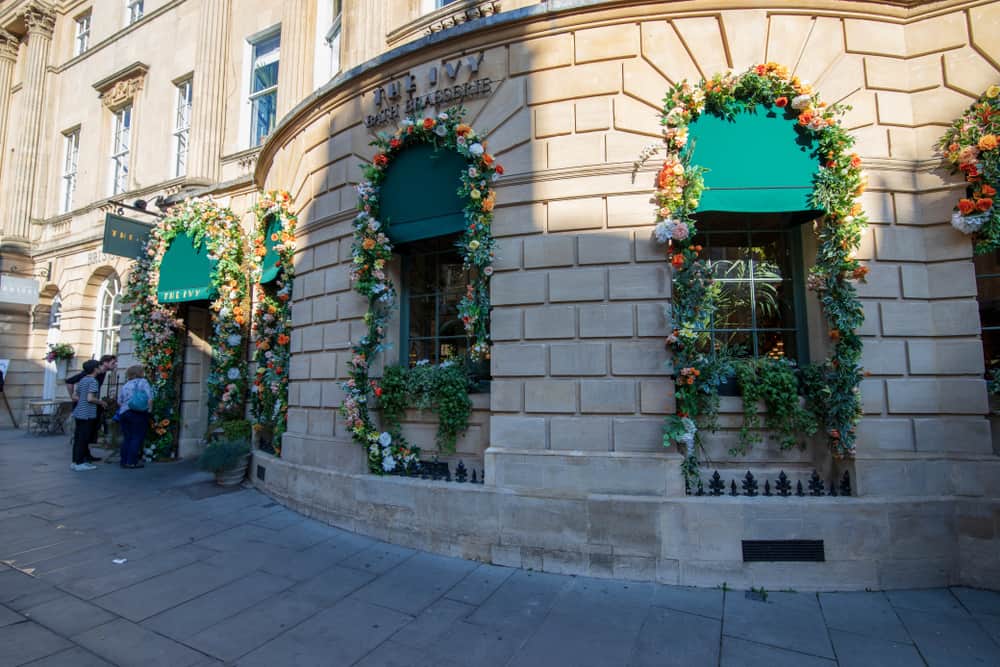 Exterior of a tan stone building that says \"The Ivy.\" Flowers are used to decorate the windows.