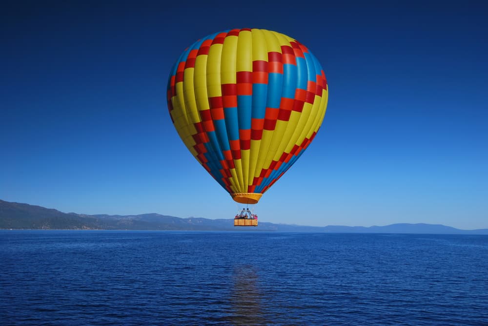 A red, yellow, and blue hot air balloon floats over the ocean.
