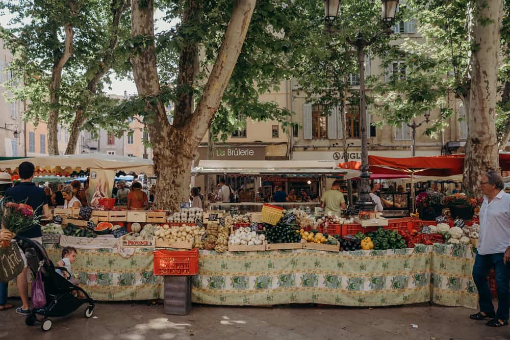 People shopping at a farmer\'s market on a busy street in France.