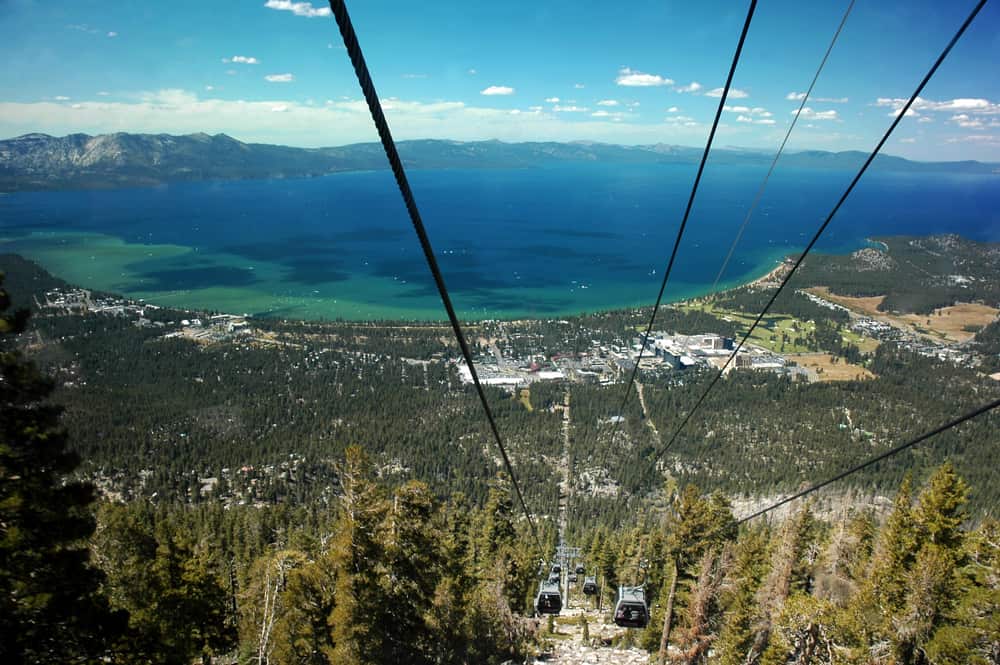 Gondolas go down a mountain with a blue lake in the background.