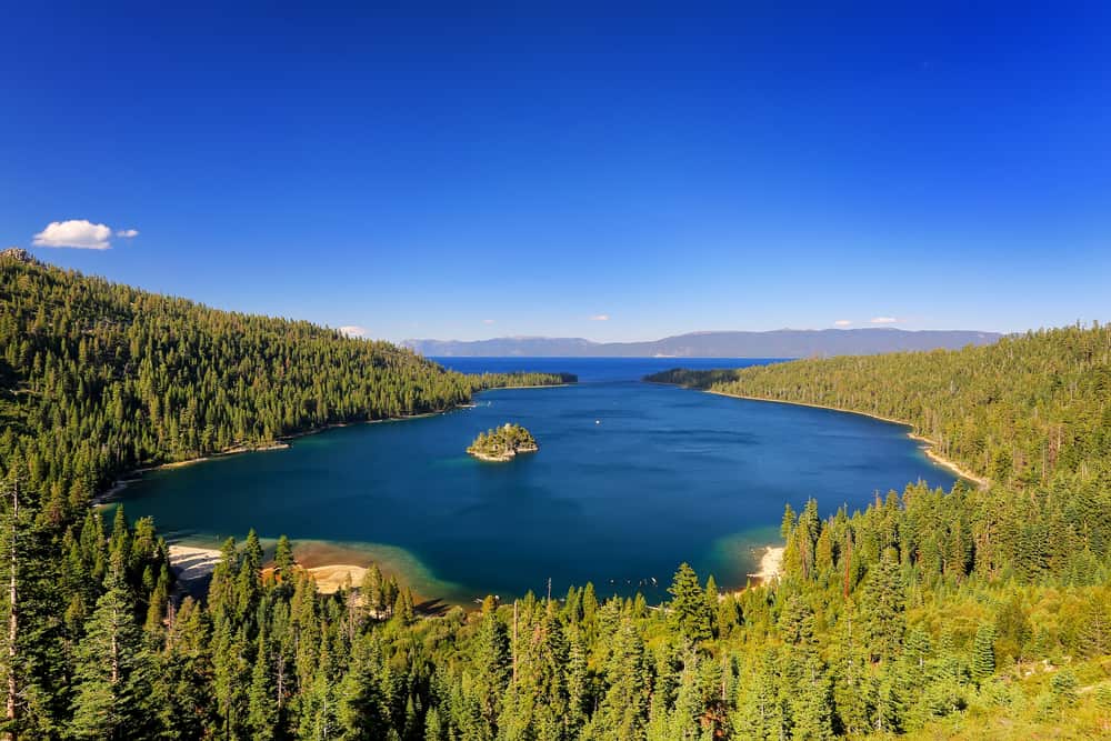 Trees line the outside of a lake with mountains in the background.