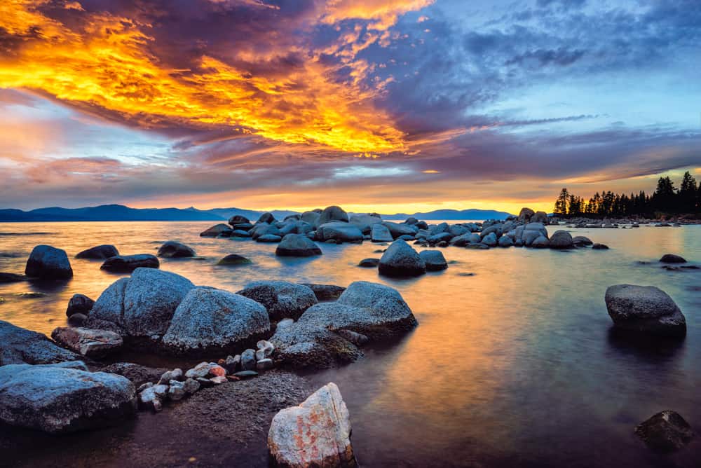 A rocky ocean sits under a purple and orange fiery sky.