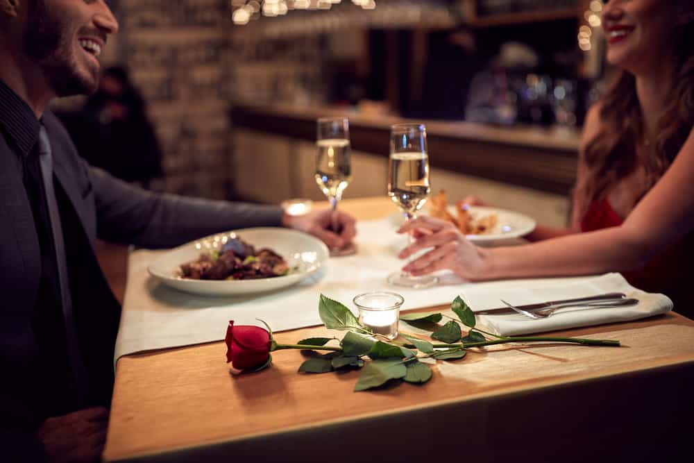 Two people enjoy a romantic dinner with a rose on the table.