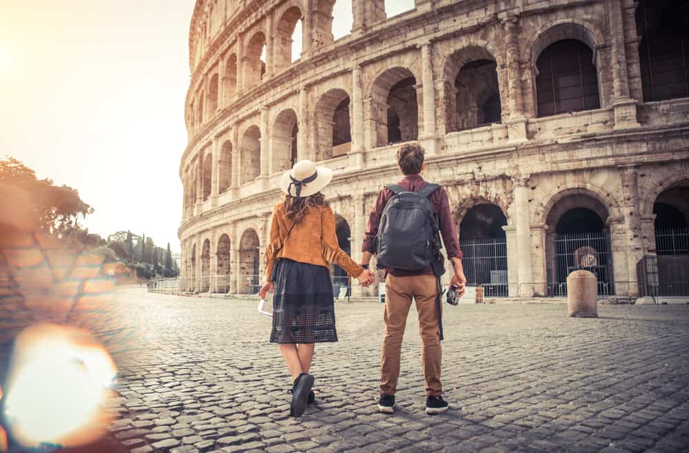 A couple holds hands in front of the Rome Colosseum.