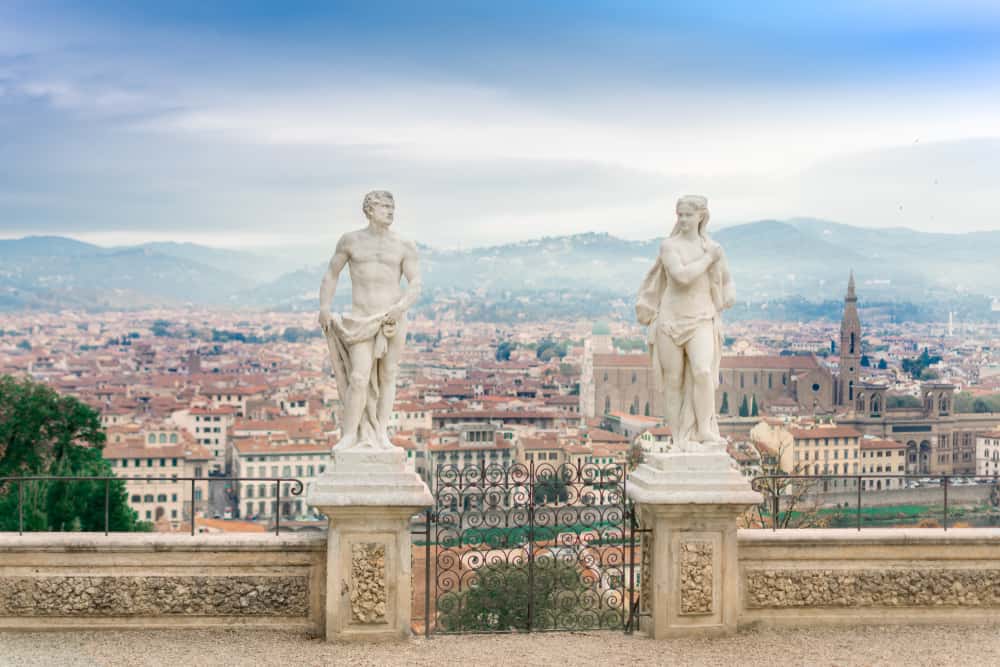 Two tall statues stand with an aerial view of a city behind.