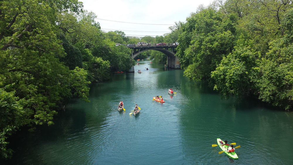 People kayak in a river under a blue sky.