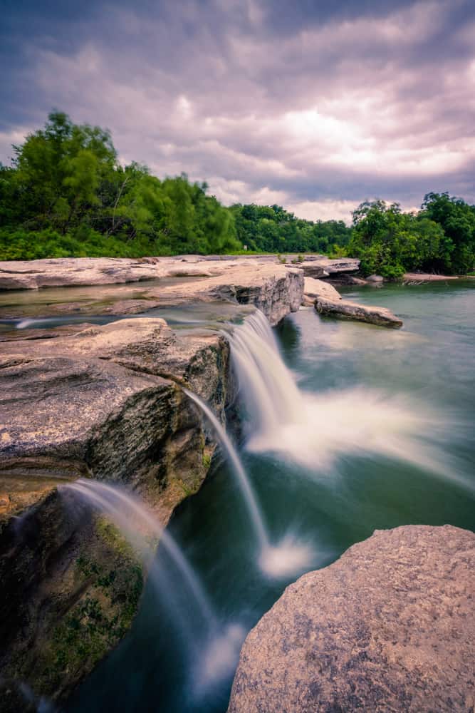 Water falls into a pool of water under a cloudy sky.