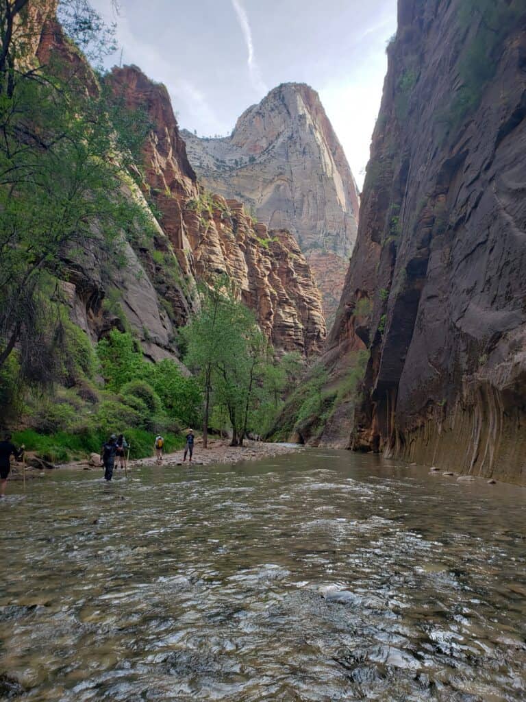 People walking along the bottom of a canyon floor that is mostly underwater. 