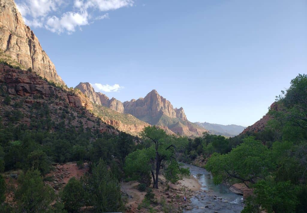 Small river flowing through the bottom of a rock canyon with green trees on either side of it. 