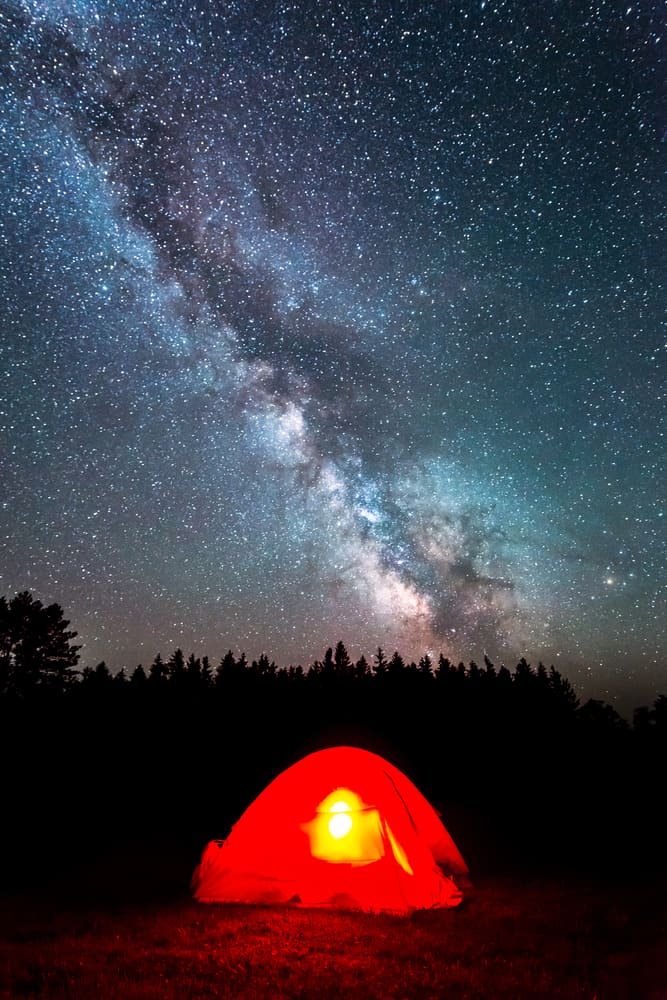 A bright red tent is seen under the milky way.