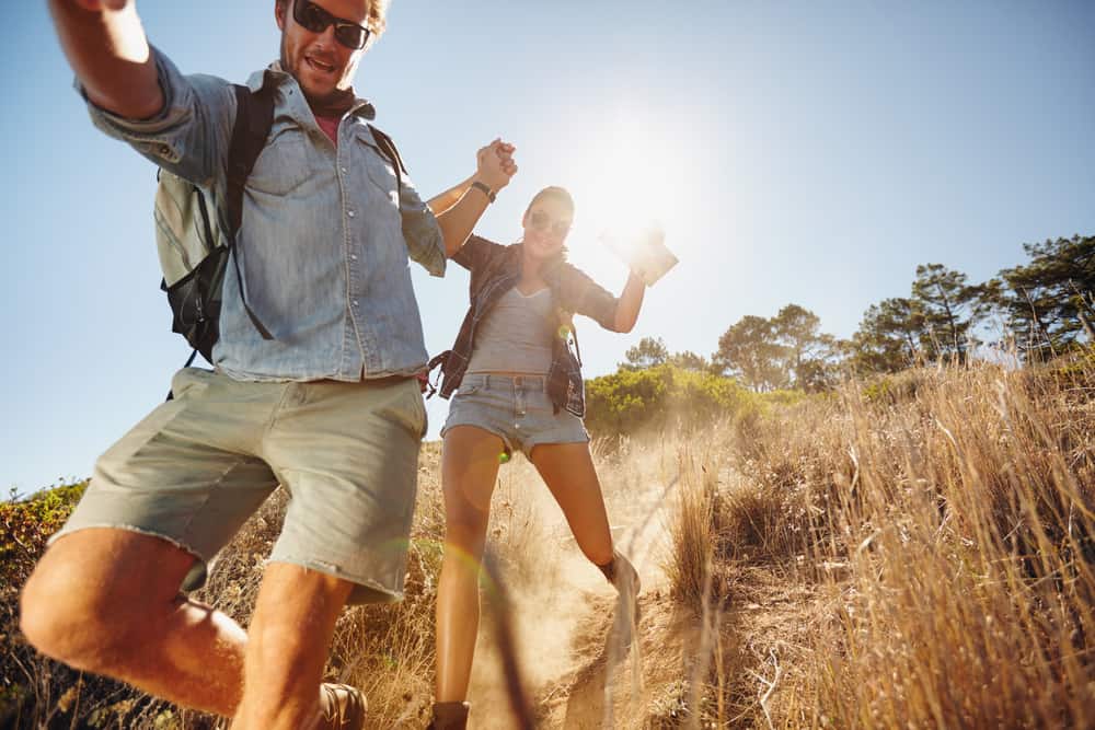 A man and woman laugh while hiking outdoors.