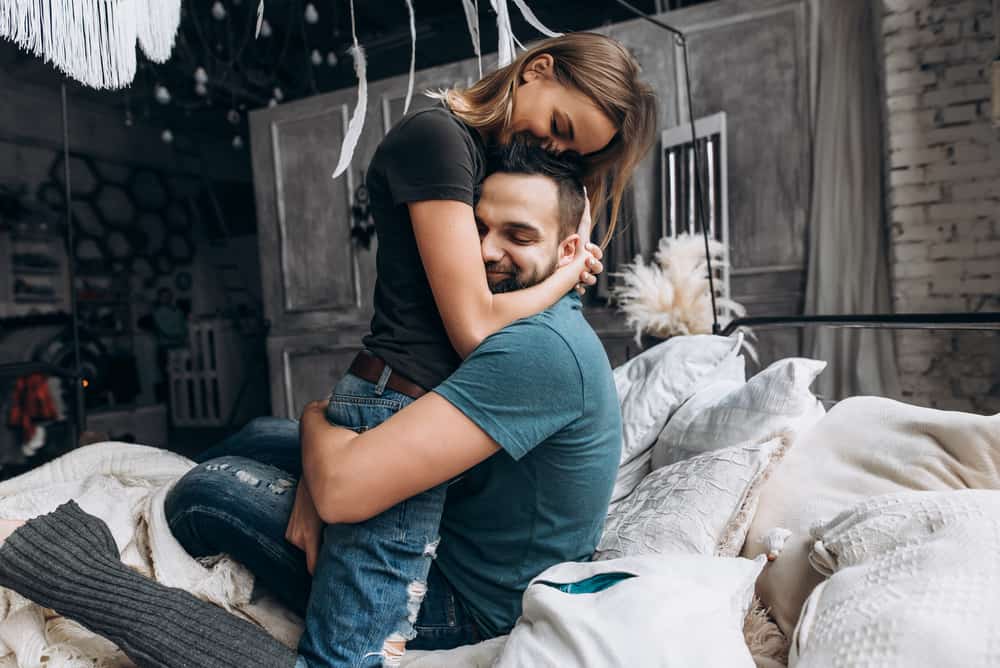 A man and woman embrace on a bed.