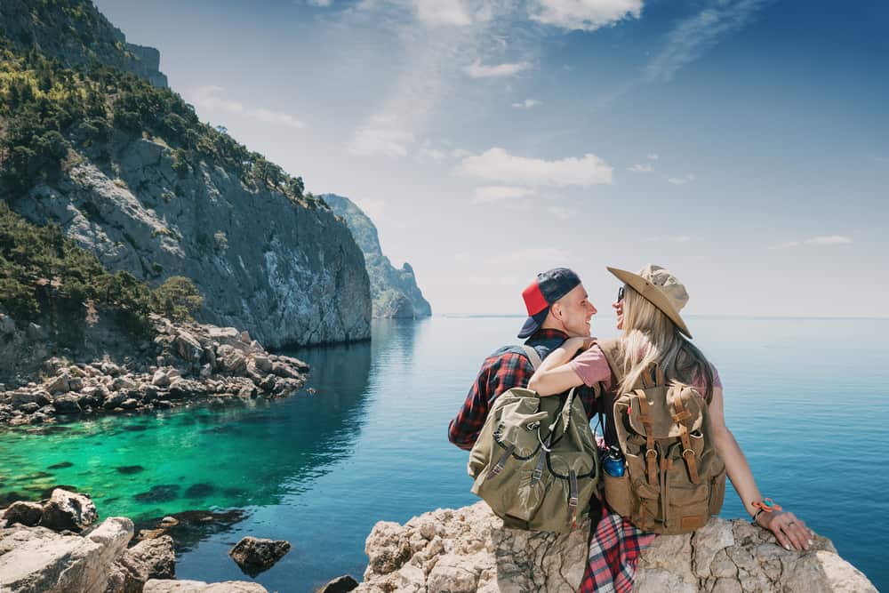 A man and woman sit looking out at the ocean on a hike.