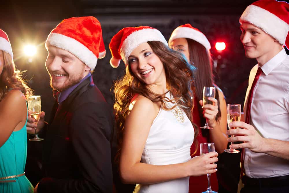 People dance with Santa hats on while holding wine.