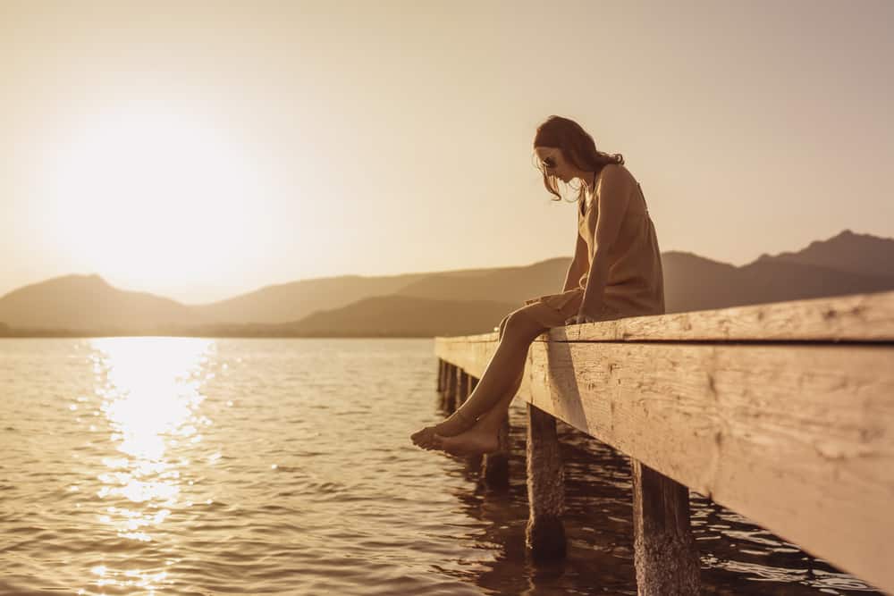 A woman sits on a wooden pier by the lake deep in thought.