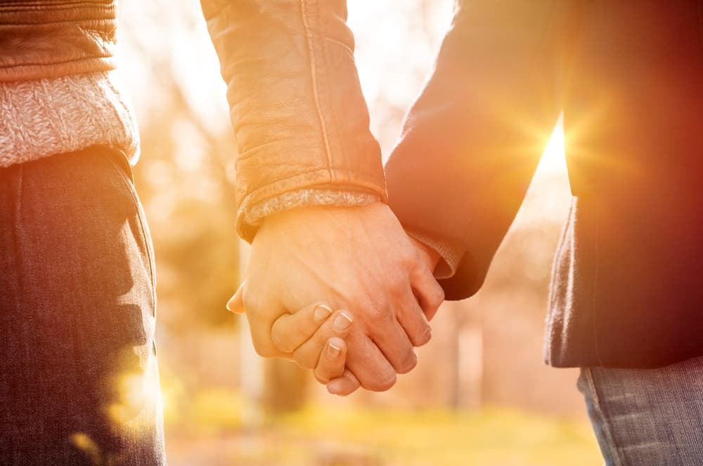 Close up of a couple holding hands as the sun shines behind them.