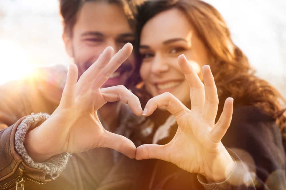 A man and woman make a heart with their hands.