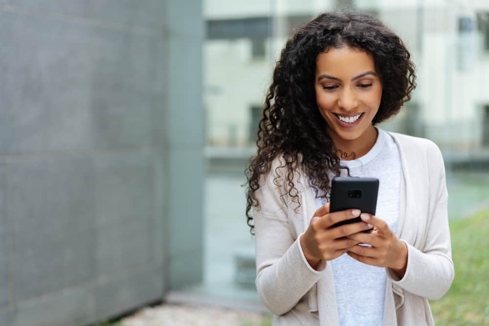 A woman is smiling outdoors on her phone.