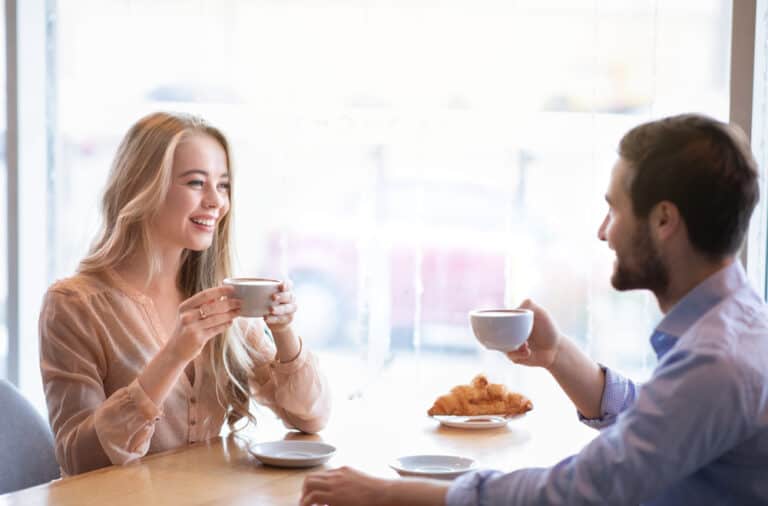 A couple is chatting while each holding a mug at a cafe.