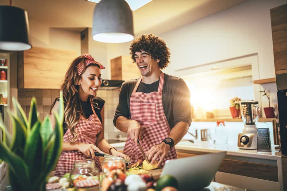 A couple laughs while cooking in a kitchen.