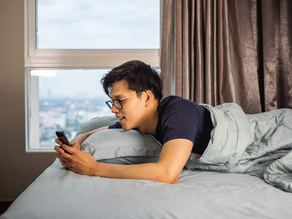 Man laying in bed smiling as he reads on his phone.