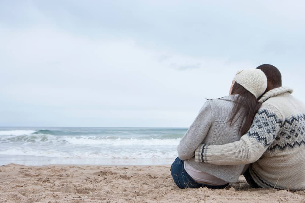 A couple is snuggled up against one another on the beach.