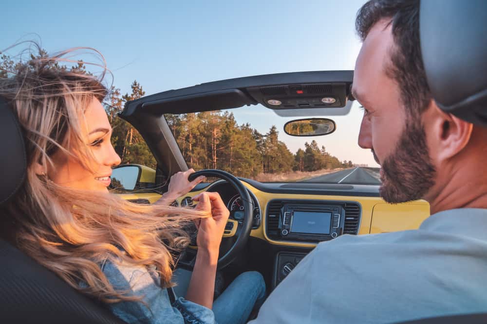 Couple smiling at each other while driving in a yellow convertible.