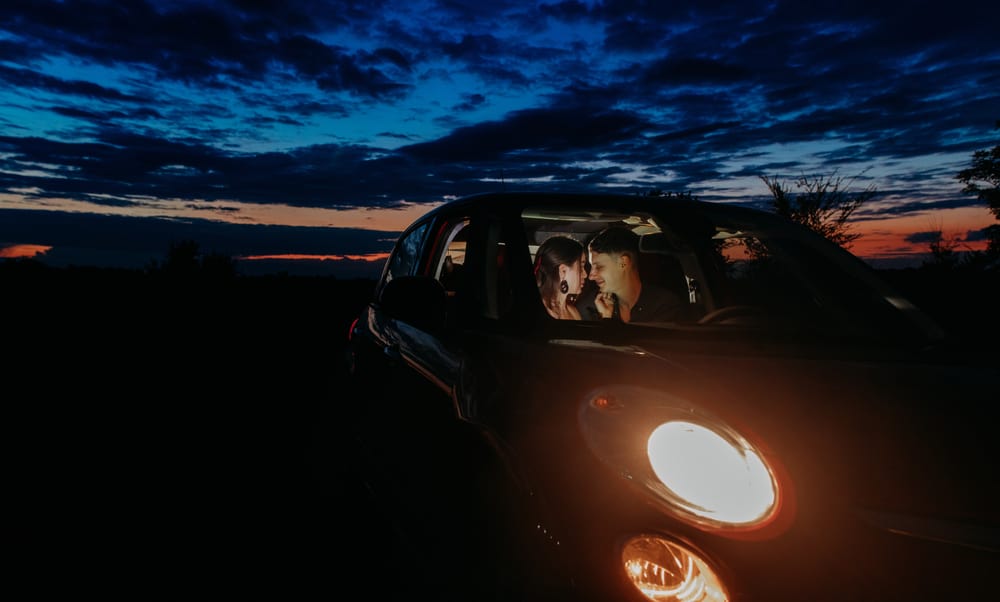 A couple kisses inside a car at night.