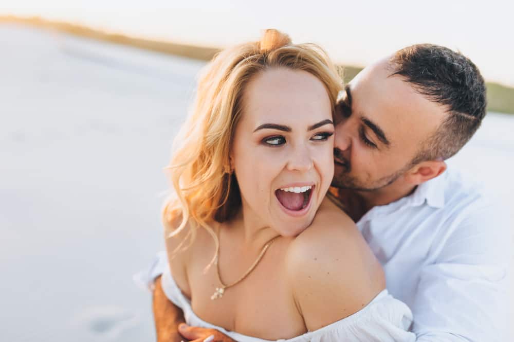 A man holds a woman from behind while they both laugh.