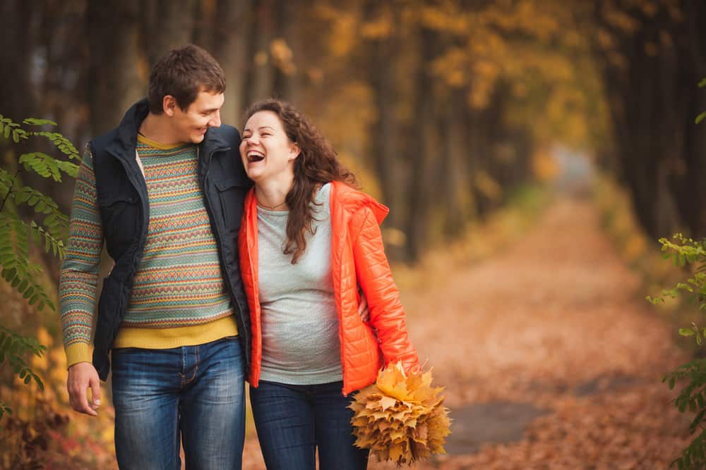 A man and pregnant woman walk outdoors surrounded by fall foliage.