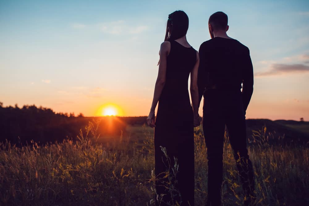 A couple stands hand in hand while watching the sunset.