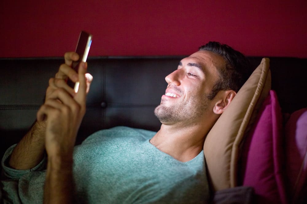 Smiling man laying on couch looking at something on his phone.