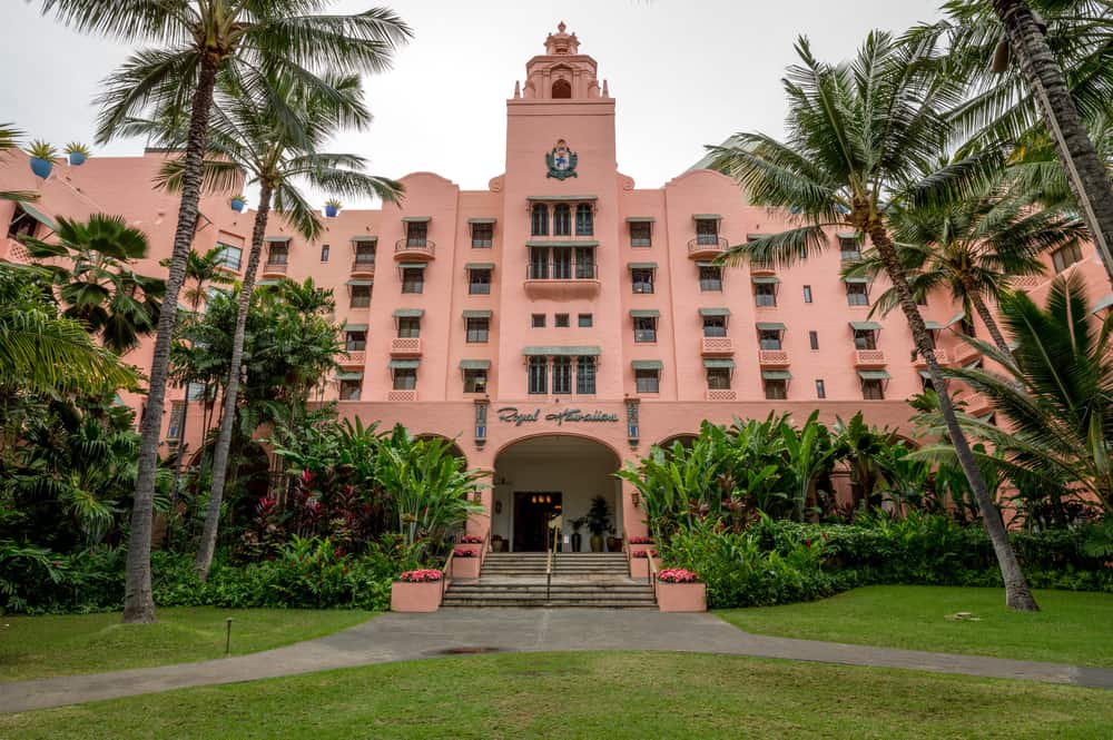 Bright pink Royal Hawaiian Hotel with lush tropical palm trees around