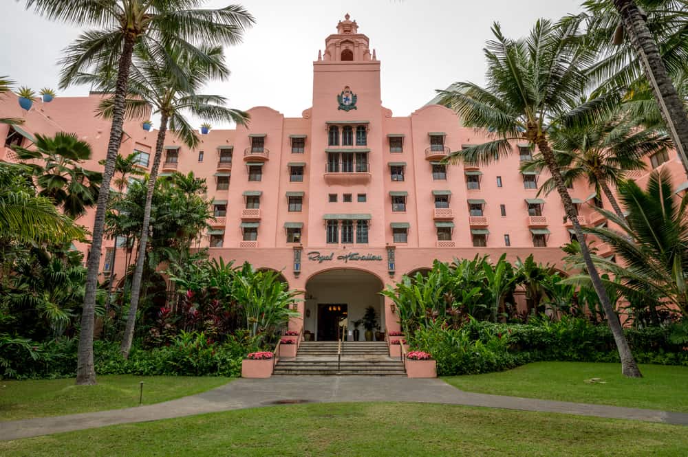 Bright pink Royal Hawaiian hotel with lush tropical palm trees surrounding it