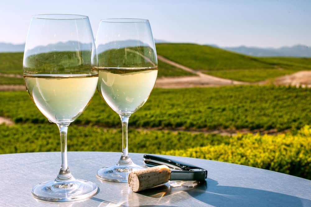 Two corked white wine glasses on table with California wine country in background under clear blue sky