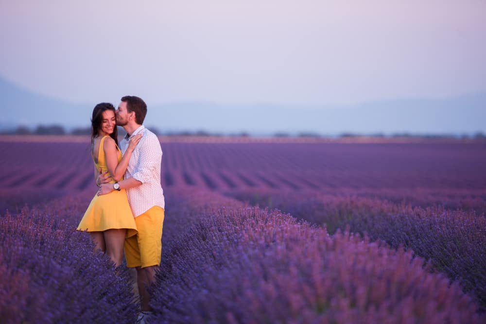 Man kissing a woman on the cheek as she smiles at the camera in a vibrant purple field of lavender