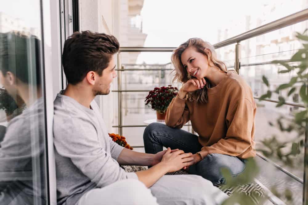 A couple sits on a balcony while chatting with each other.