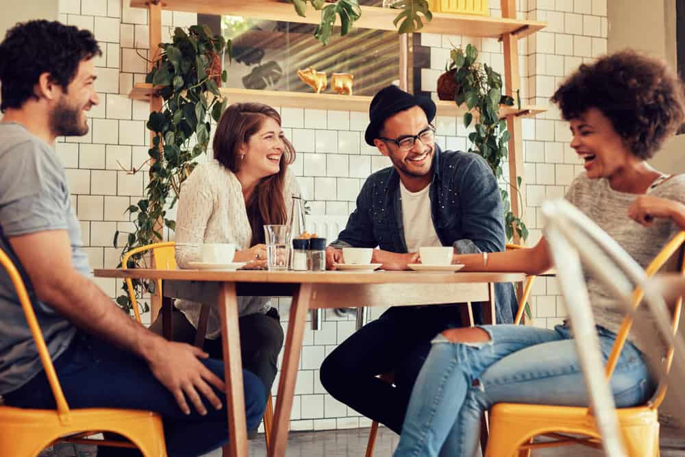 Vier Freunde sitzen herum ein Tisch in einem Restaurant, der einander anlächelt und lacht