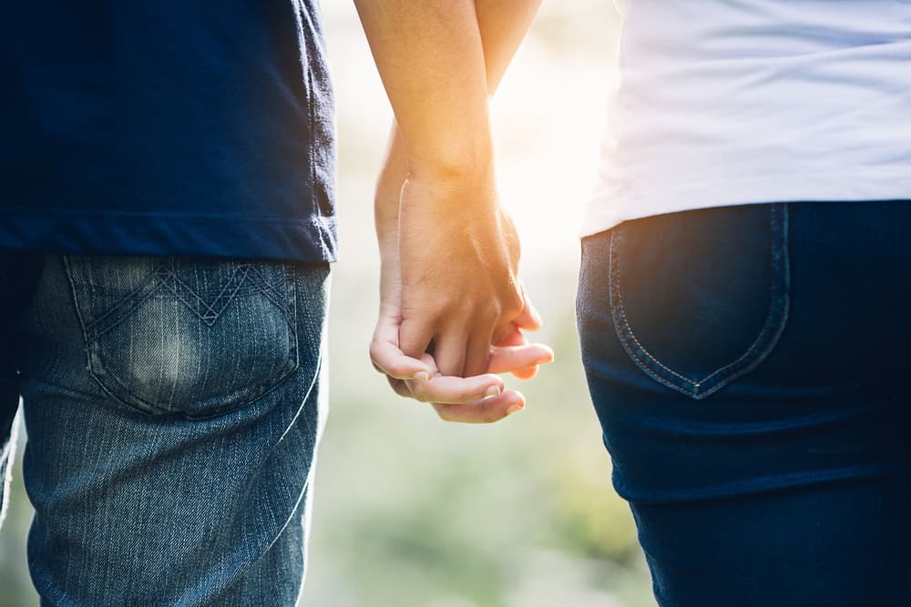 A close up of a couple holding hands being silhouetted by a sunburst in the background