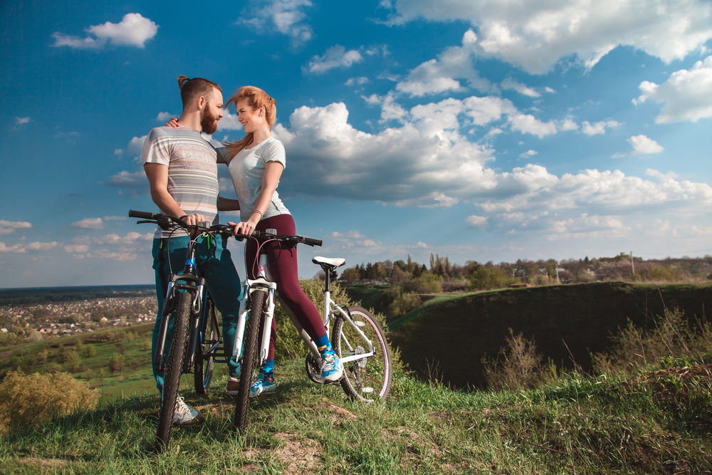 A couple on bikes give each other an intimate embrace surrounded by greenery.
