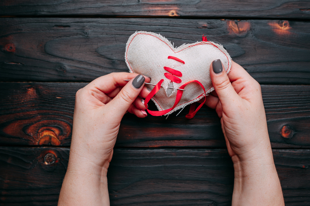 A close up of a woman's hands sewing together a broken heart