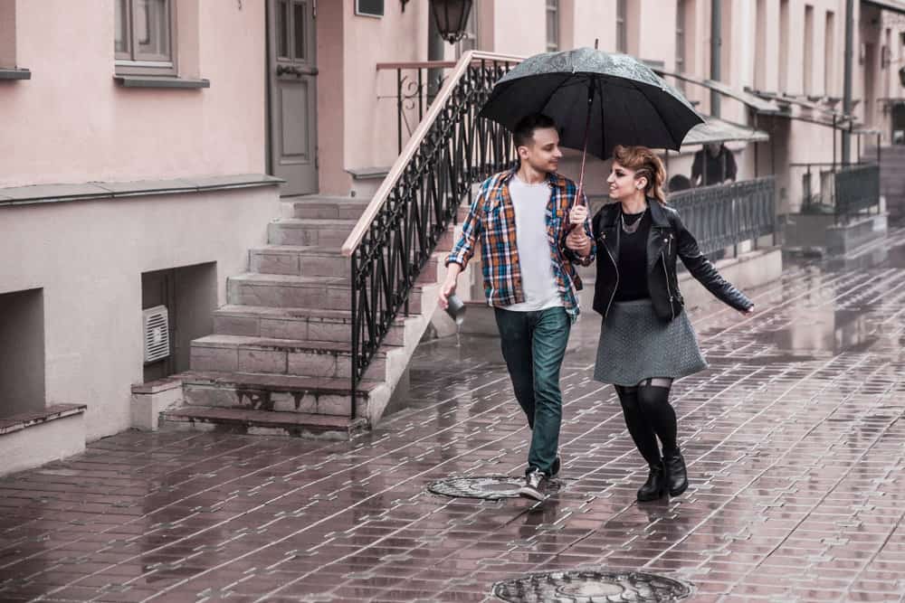 A couple walks outdoors in the rain while sharing an umbrella.