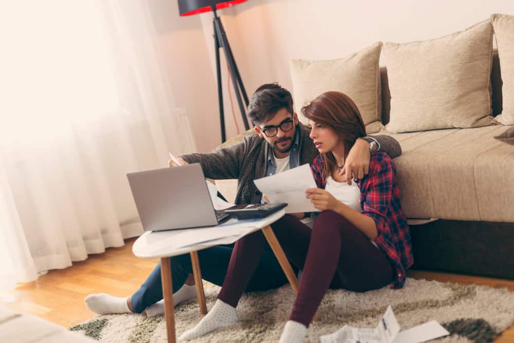 A couple sits while looking at bills on their laptop.